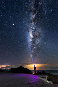 Silhouette person flashing light while standing on beach against sky at night