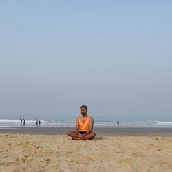 Man sitting at beach against clear sky