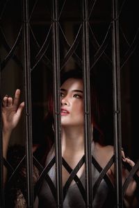 Portrait of young woman looking through metal fence