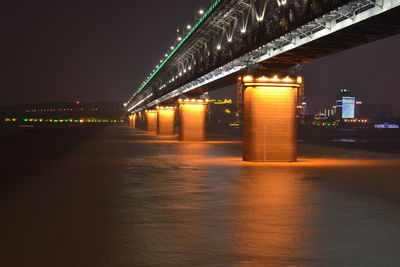 Illuminated bridge over river against sky at night