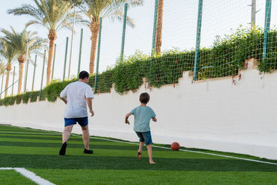 Man with boy playing football on green sports field.