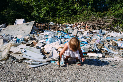 Little girl at a dump among a heap of scattered garbage in the forest.