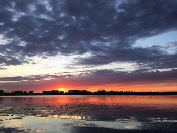 Scenic view of lake against dramatic sky during sunset