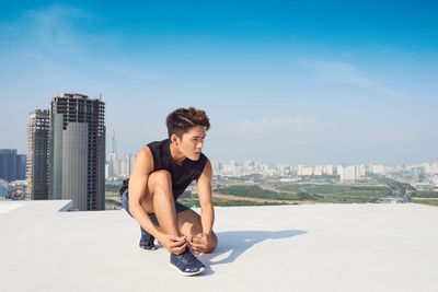 Young man sitting on woman against sky in city