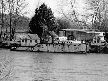 Boats in river by bare trees against sky