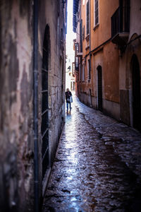 Rear view of man walking on narrow alley amidst buildings