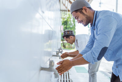 Side view of smiling man washing hands in mosque