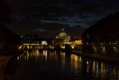 Illuminated buildings by river against sky at night