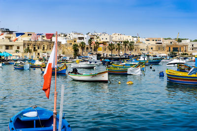 Boats moored in canal by buildings against blue sky