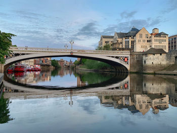 Bridge over river by buildings against sky in city