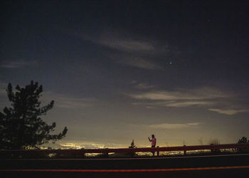 Road by silhouette trees against sky at night