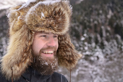 Man in a fur winter hat with ears smiling portrait on a background of a winter forest