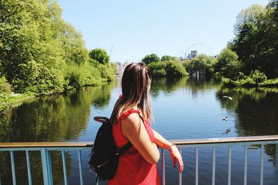 Side view of backpack woman standing on bridge over river against clear sky