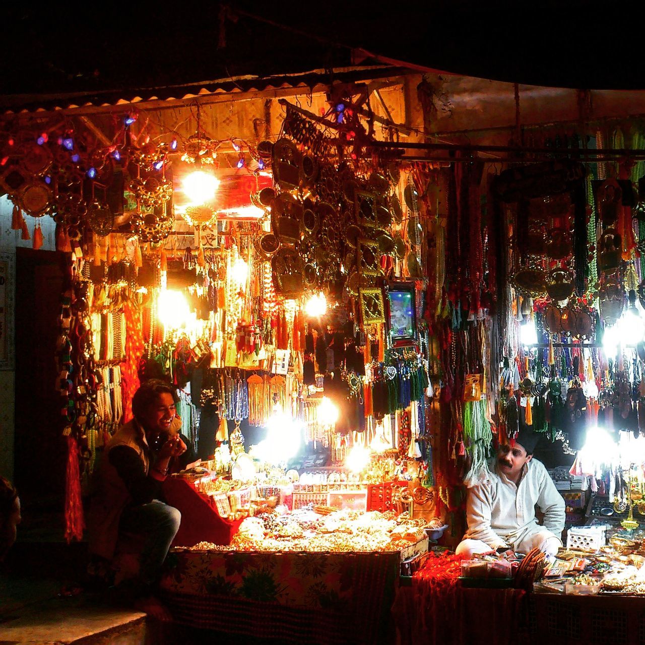 REAR VIEW OF PEOPLE SITTING AT ILLUMINATED NIGHTCLUB