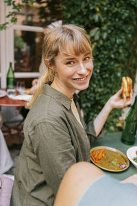 Side view of smiling young woman sitting with food at restaurant