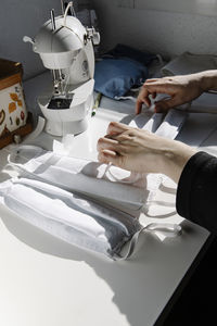 Crop female tailor making face masks with fabric and rubber bands