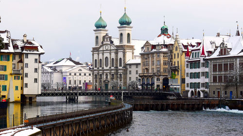 View of buildings by river in city against sky
