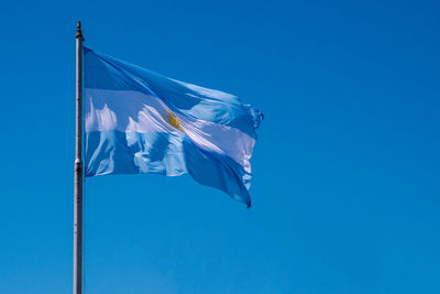 Low angle view of argentinian flag waving against clear blue sky