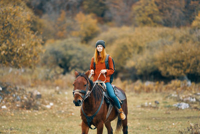 Portrait of young woman riding horse on field