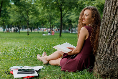 Full length of woman with open book sitting on grass