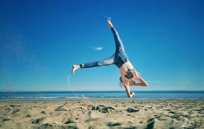 Upside down image of man on beach against blue sky