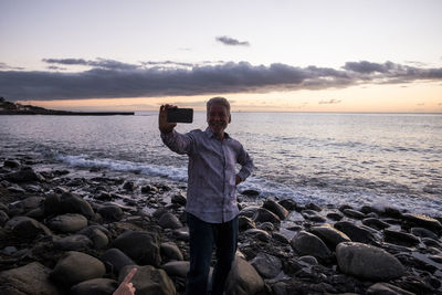 Man photographing from mobile phone at beach during sunset