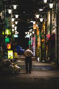 Rear view of woman walking on illuminated street at night