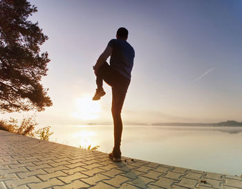Active sport man runner stretching body on pavement lake side, regular outdoor training for marathon