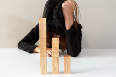 Sad woman with head in hand sitting by stacked wooden blocks on table