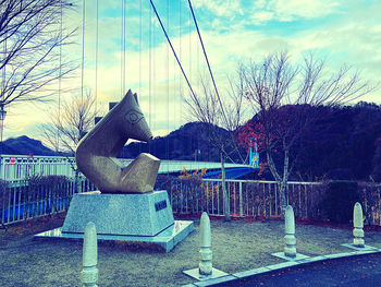 Statue by bare tree in park against sky