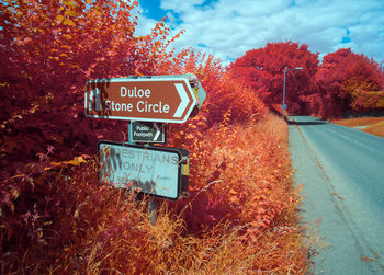 Road sign by trees against sky