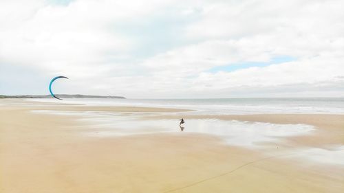 High angle view of man kiteboarding on beach against cloudy sky