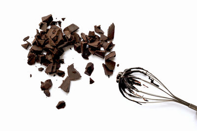 Broken chocolates and wire whisk on white background