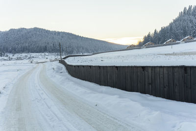 Snow covered landscape against sky during sunset