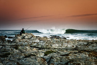 Silhouette man fishing by sea against sky during sunset