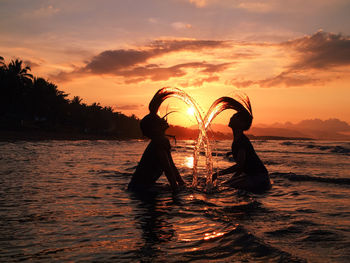 Silhouette people in sea against sky during sunset