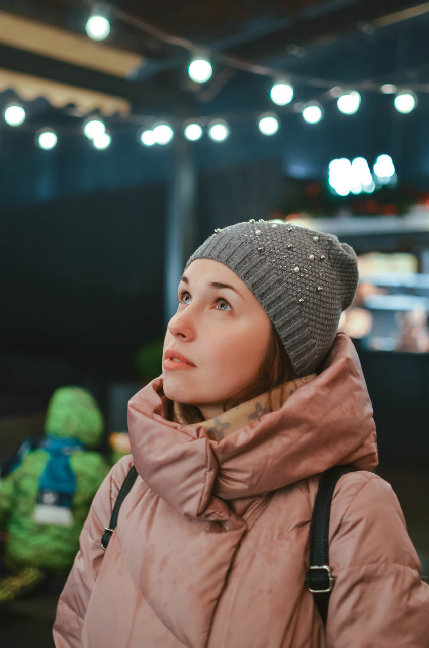 one person, real people, clothing, focus on foreground, looking away, lifestyles, looking, leisure activity, portrait, indoors, winter, illuminated, young adult, warm clothing, hat, women, standing, headshot, front view, contemplation, beautiful woman, scarf, hairstyle