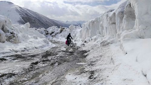 Person riding bicycle on snowcapped mountain against sky
