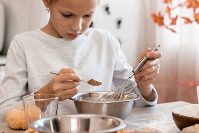 Treats and preparations for the celebration of halloween. cute little girl adds ginger to baking 