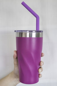 Cropped hand of woman holding purple drinking glass against wall