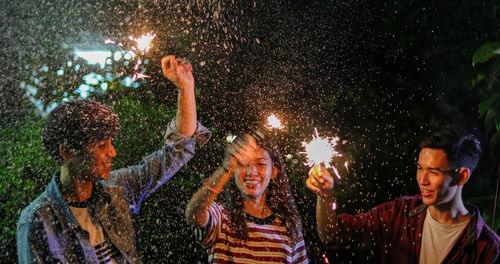Happy friends holding sparklers at night