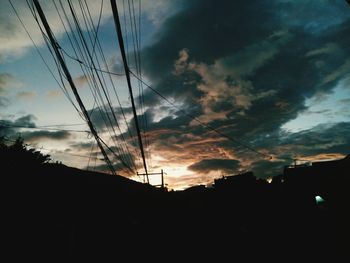 Silhouette trees and electricity pylon against dramatic sky