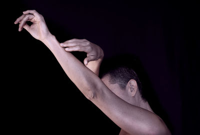 Side view of man with arms raised against black background