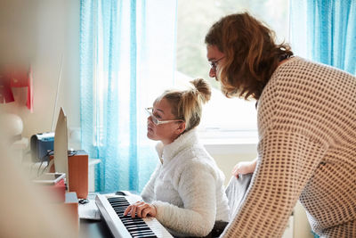 Male caretaker with disabled woman playing piano at home