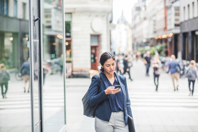 Businesswoman using phone while standing in city