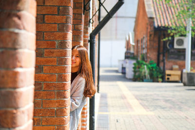 Portrait of young woman standing behind brick wall
