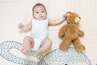 Asian baby healthy boy lying with bear toy on play blanket at home.