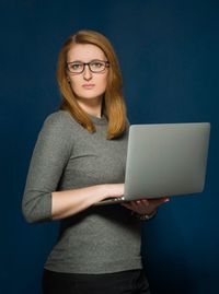 Portrait of young woman using laptop against blue background