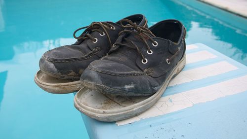 Close-up of damaged shoes on diving board against swimming pool