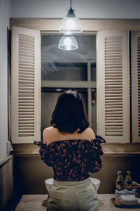 Rear view of woman standing against window